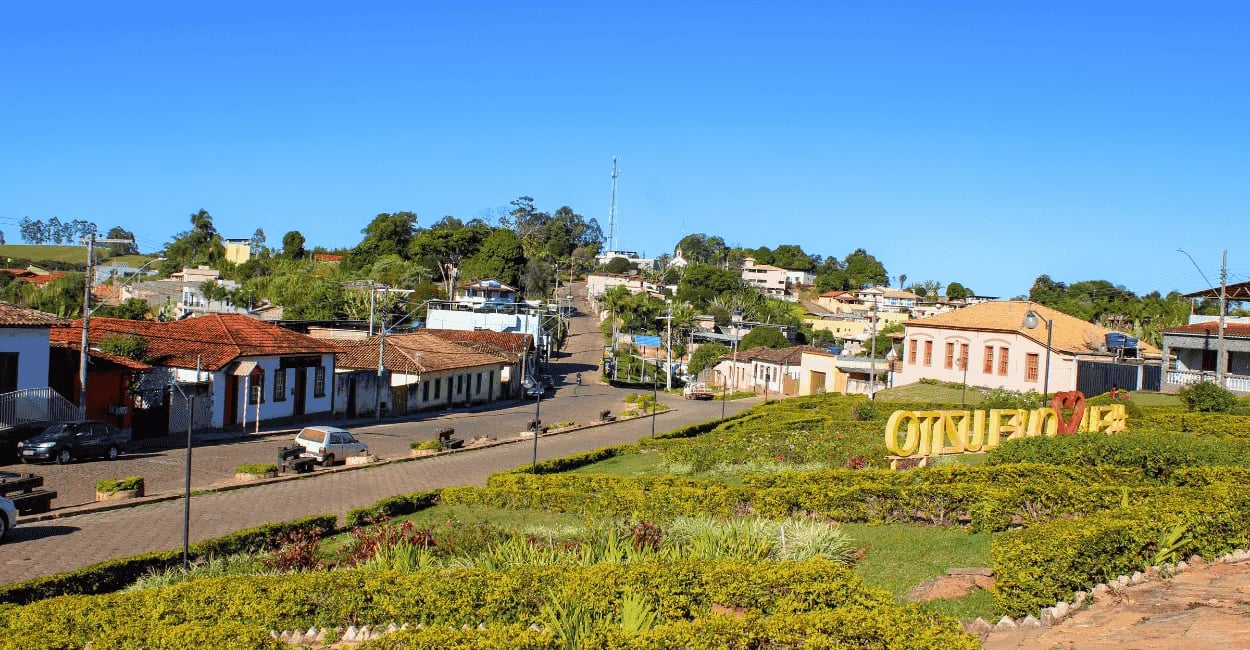 Vista panorâmica de Queluzito com praça ajardinada, letreiro turístico e casas ao redor