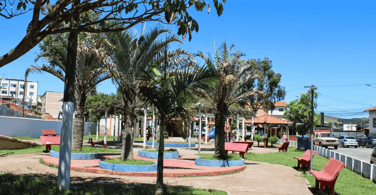 Praça em frente à antiga estação ferroviária de Carandaí com palmeiras, bancos coloridos e área infa