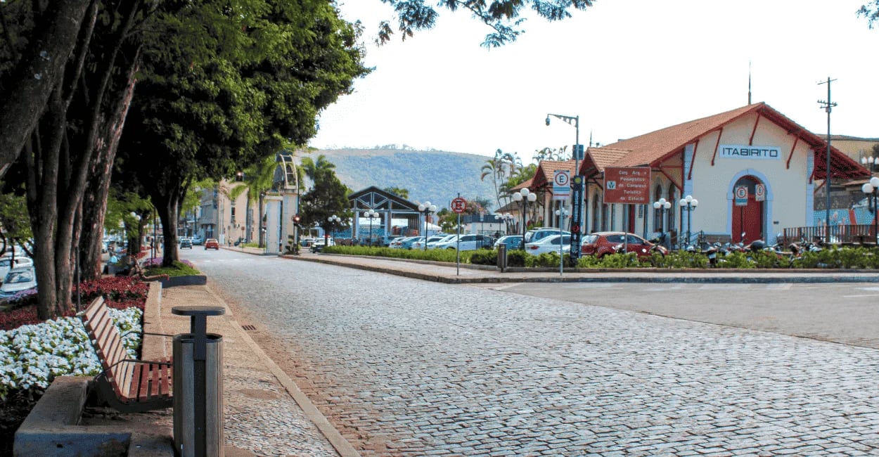 Rua em Itabirito com calçamento de pedra, estação ferroviária, bancos e árvores na praça central
