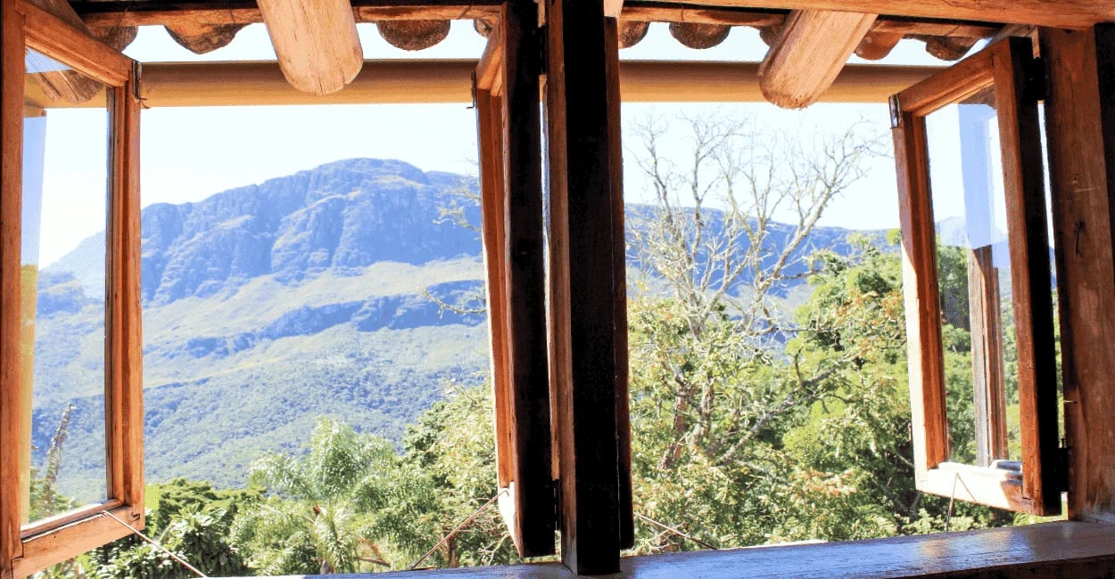Vista das montanhas de Itatiaia MG pela janela de uma casa rústica, cercada por natureza verde