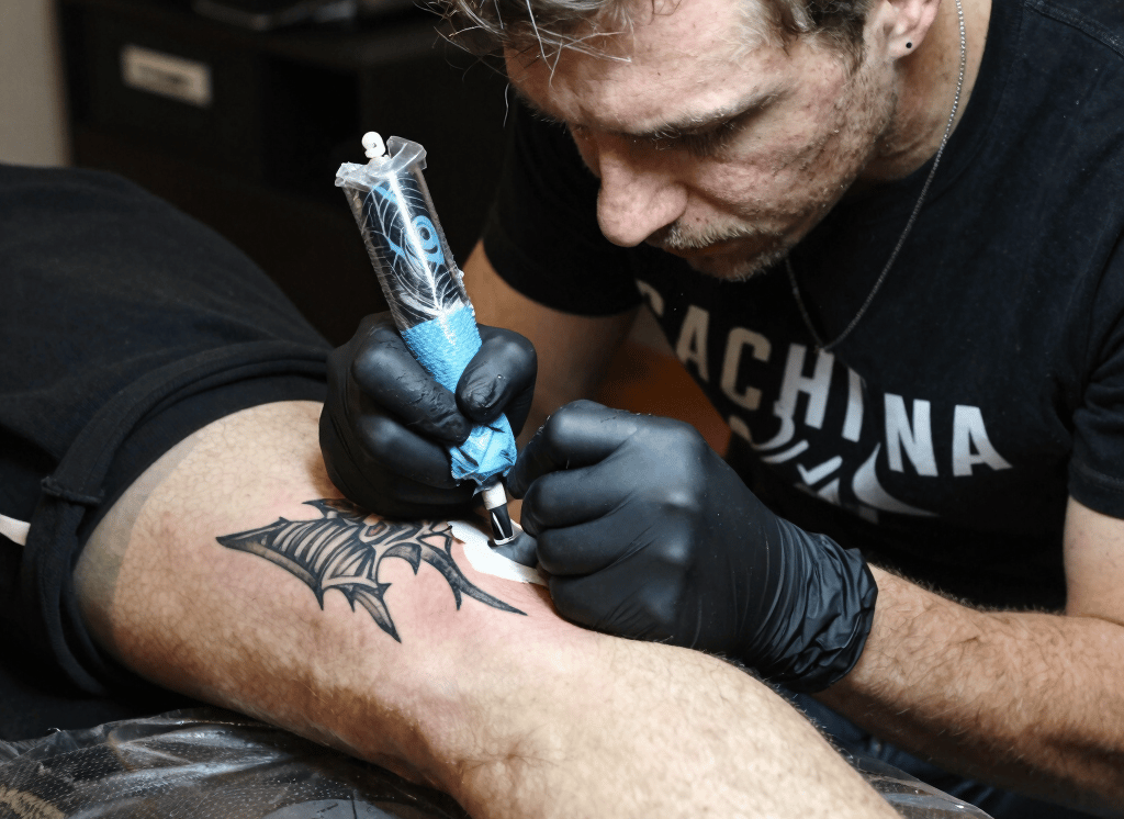 Close-up of a tattoo artist working meticulously on a client's skin in a neon-lit studio.