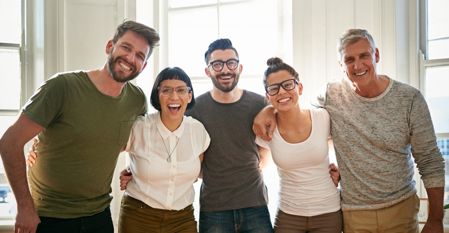 Group of young men and women smiling together with arms around each other during a team photo.