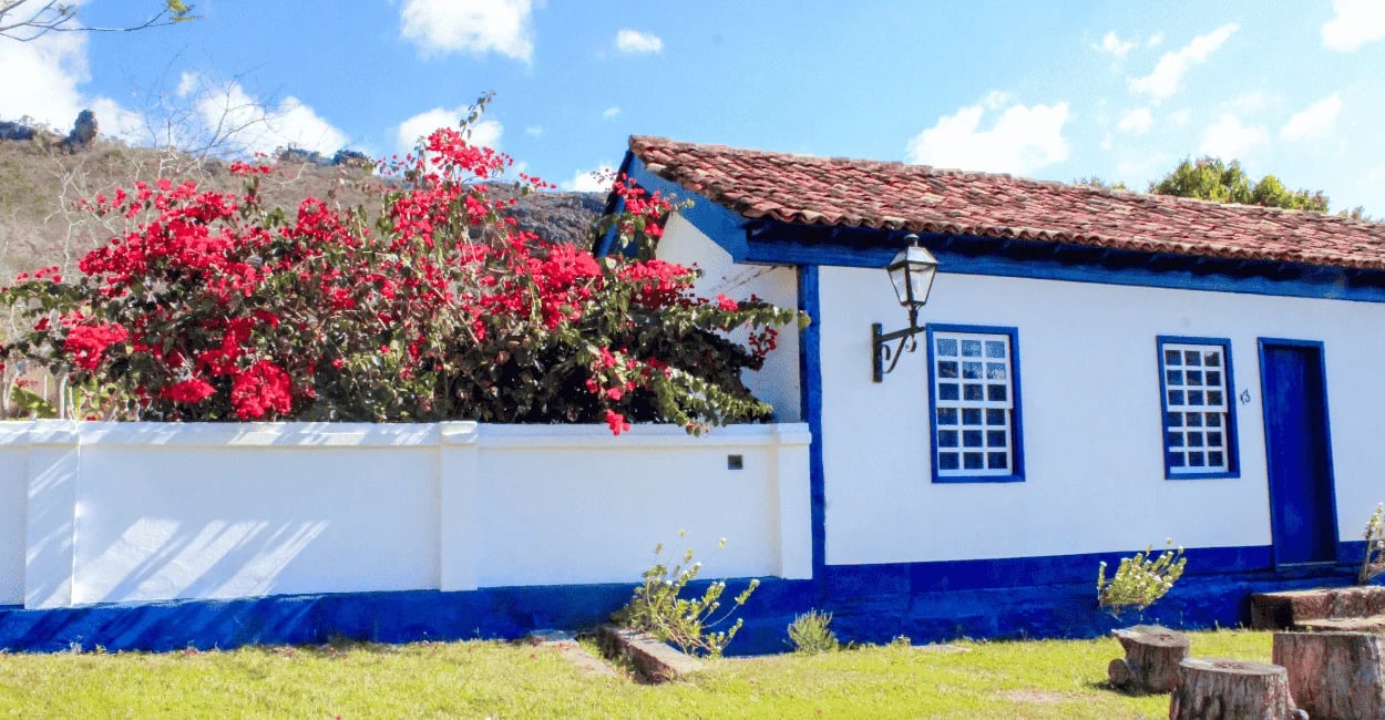 Casa colonial na Vila do Biribiri com fachada branca, detalhes azuis e flores vermelhas no jardim