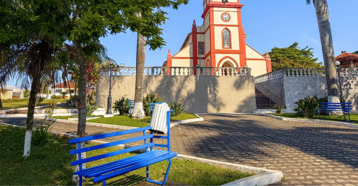 Banco azul em praça arborizada diante da Igreja Matriz de Ibituruna, em Minas Gerais