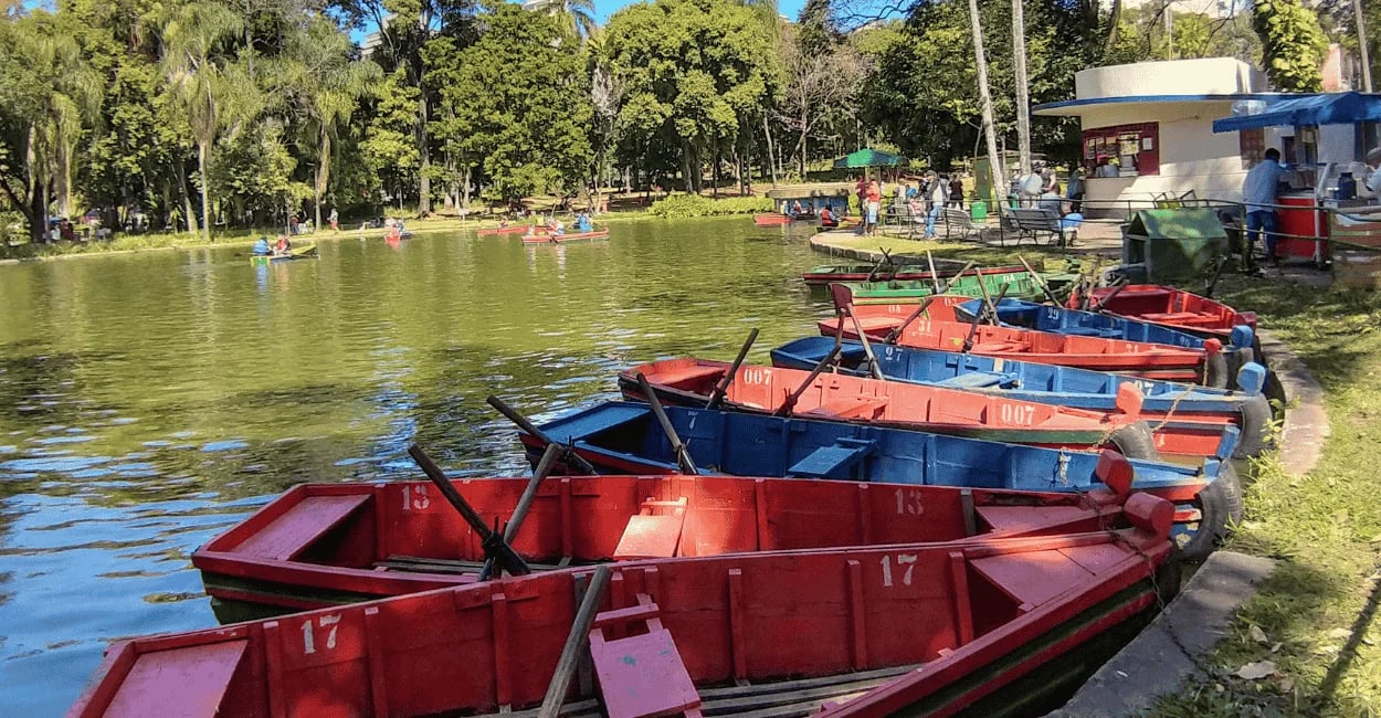 Barcos com cores azul e vermelha, com lagoa de cor verde e árvores no parque municipal de BH