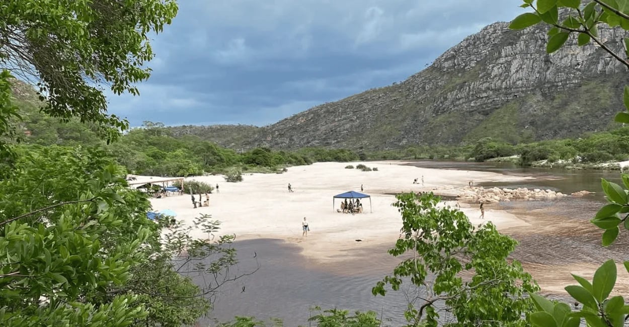 Praia da Cachoeira do Telésforo com rio, areia clara, vegetação e serra ao fundo em Conselheiro Mata