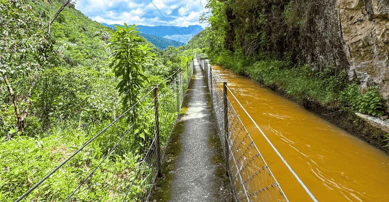 Passarela de concreto, com guarda corpo, rio do lado e montanhas e vegetação do outro em Ouro Preto