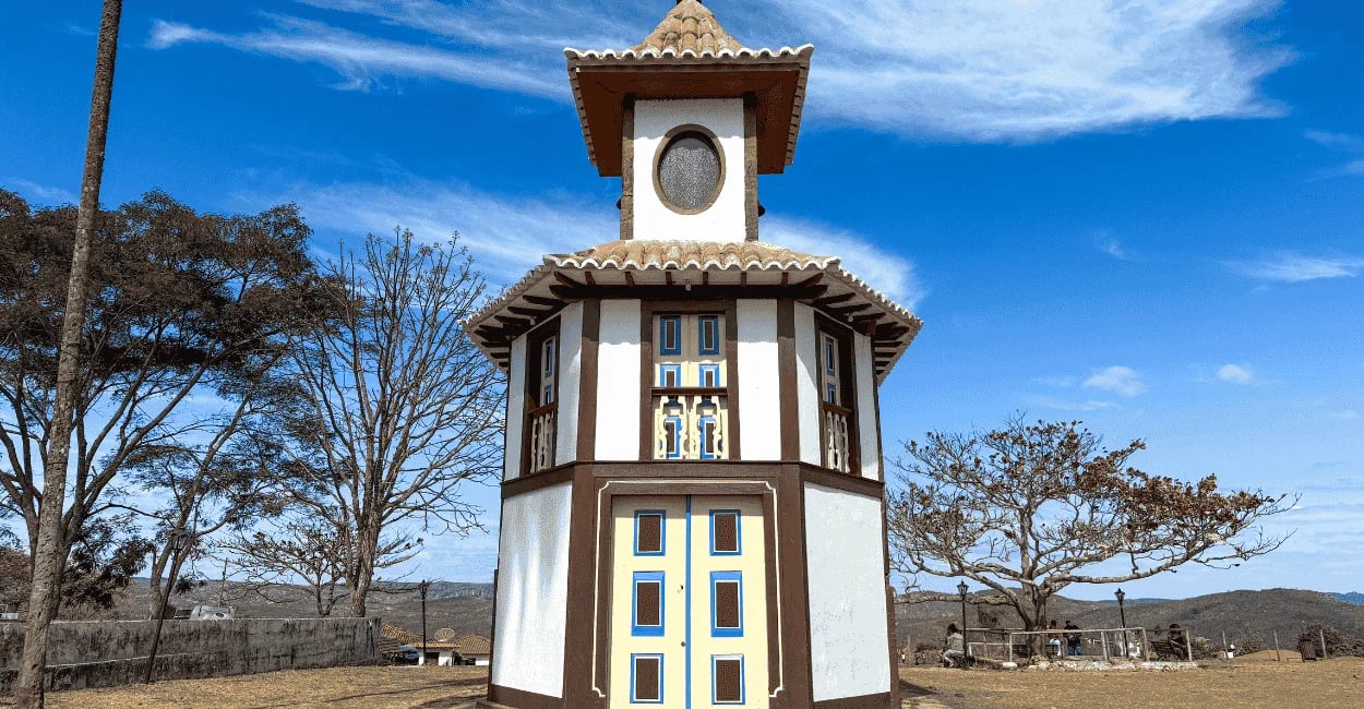 Capela de Nossa Senhora do Rosário em Milho Verde, céu azul, cor marrom e branca e árvores em volta
