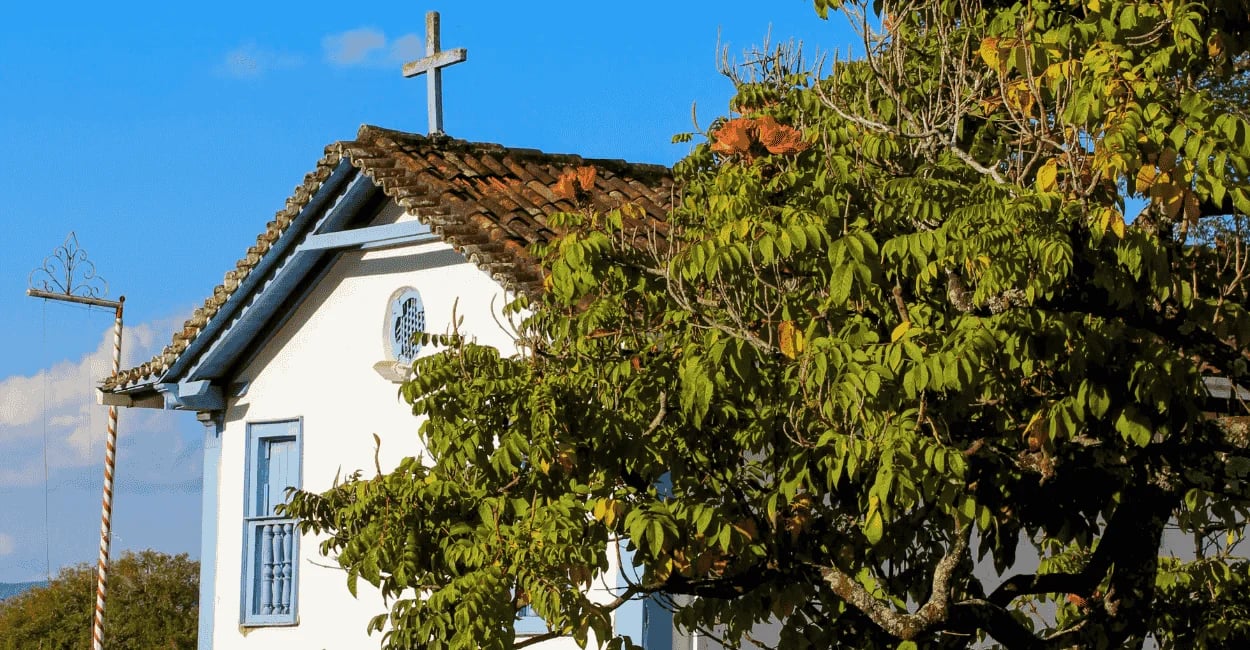 Capela em Morro d’Água Quente, com árvore ao lado, janela azul e céu claro