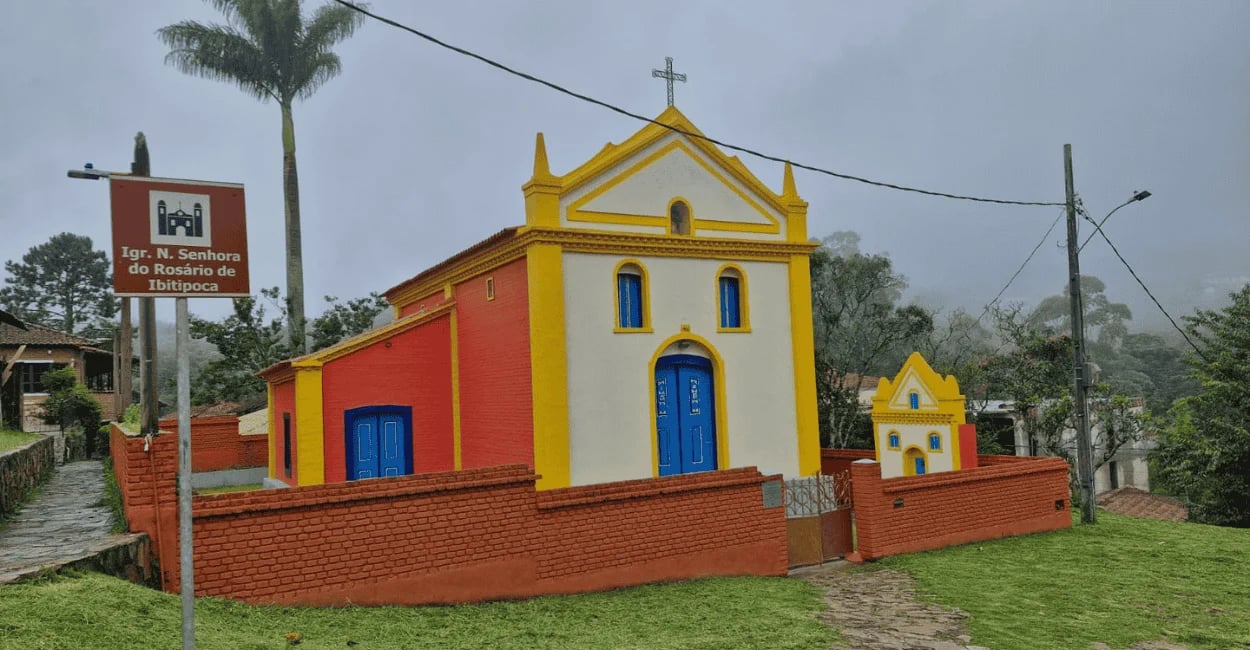 Igreja do Rosário em Ibitipoca, com fachada branca, amarela e vermelha, portas azuis e muro ao redor