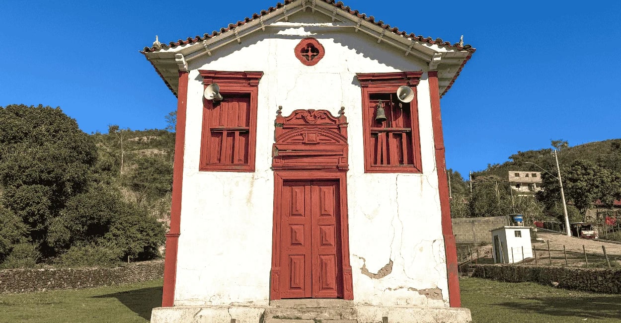 Capela em Itapanhoacanga, com fachada colonial branca e vermelha, sino e céu azul