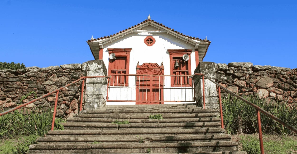 Igreja histórica em Itapanhoacanga MG com escadaria frontal, muro de pedra e céu azul ao fundo