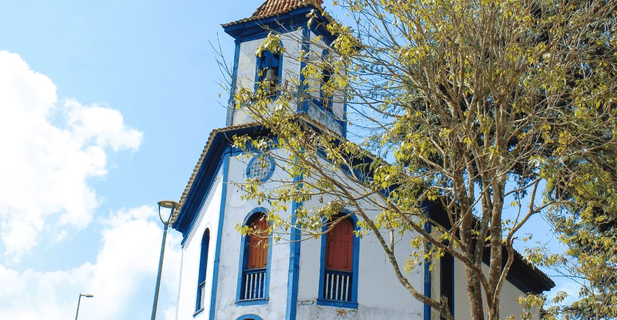 Igreja histórica em Santa Bárbara MG com detalhes azuis e árvore à frente
