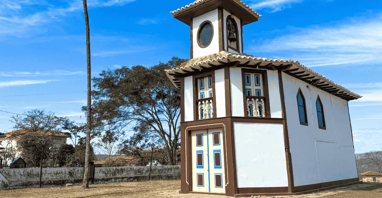 Capela do Rosário em Milho Verde, de cor branca e marrom, com vegetação tipica da região ao fundo