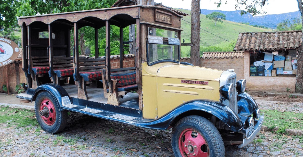 Carro antigo em frente ao Museu do Automóvel em Bichinho, com carroceria aberta e cenário rural