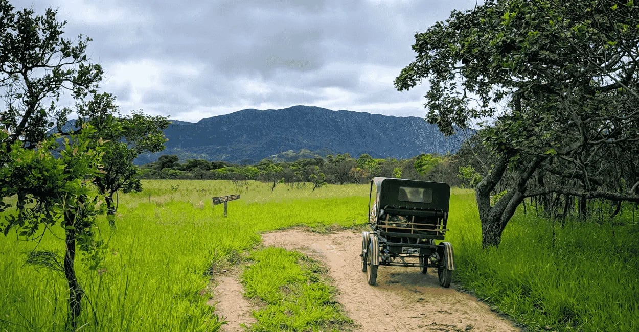 Paisagem da Serra do Cipó MG com charrete em estrada de terra, campo verde e serra ao fundo