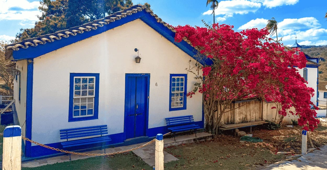 Casa histórica na Vila do Biribiri, com fachada branca e azul, bancos na frente e flores vermelhas