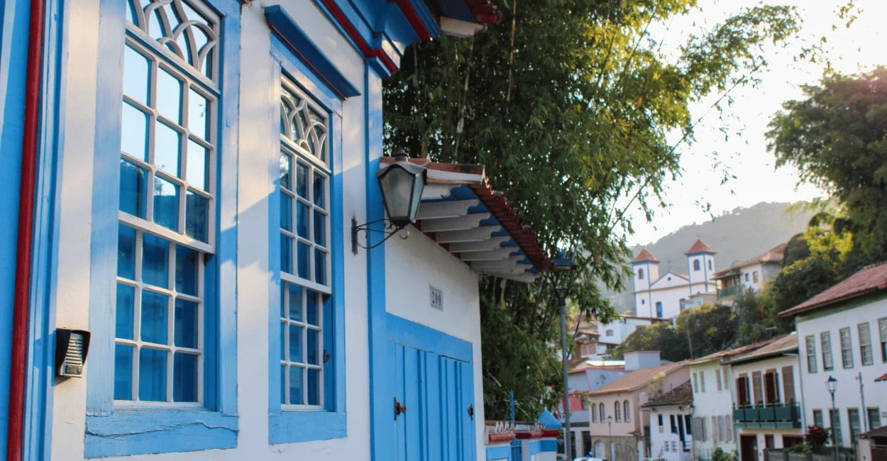 Casarão colonial com janelas azuis e igreja histórica ao fundo no centro de Sabará, Minas Gerais