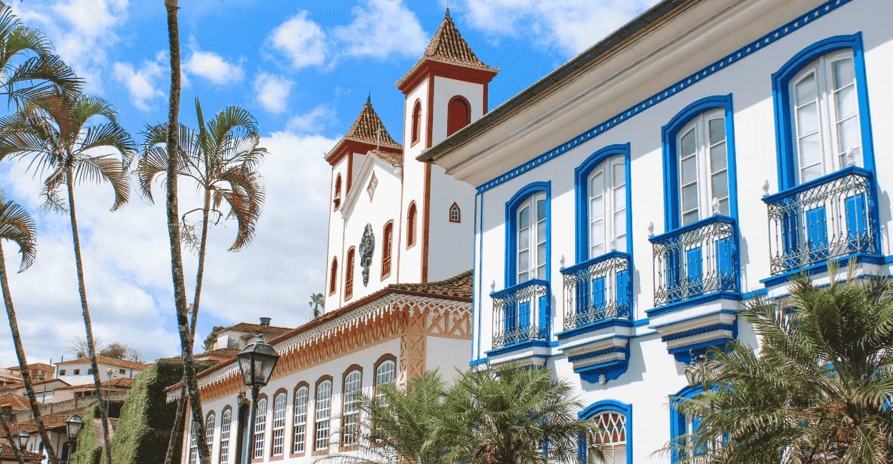 Casarões coloniais brancos com janelas azuis e uma igreja histórica ao fundo na cidade de Serro MG
