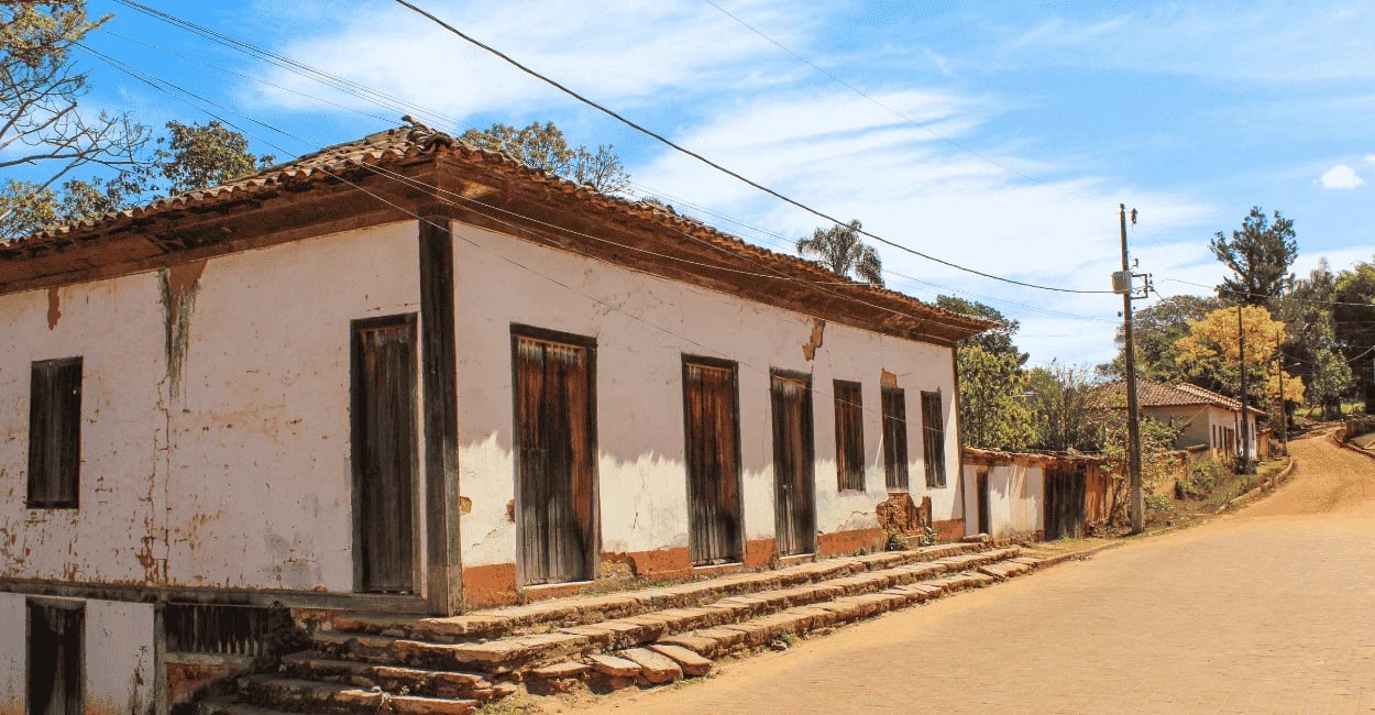 Antiga casa colonial branca com portas de madeira rústica e rua de terra em Milho Verde, Minas Gerai