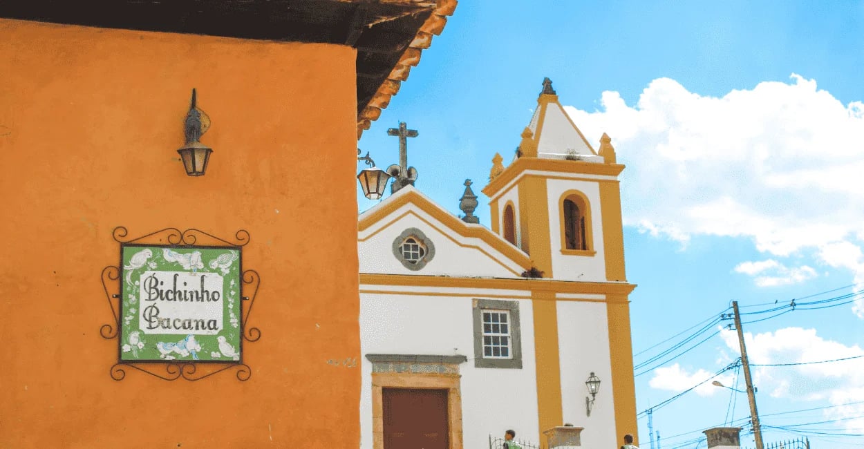 Fachada de uma casa em Bichinho MG com placa Bichinho Bacana e igreja histórica ao fundo