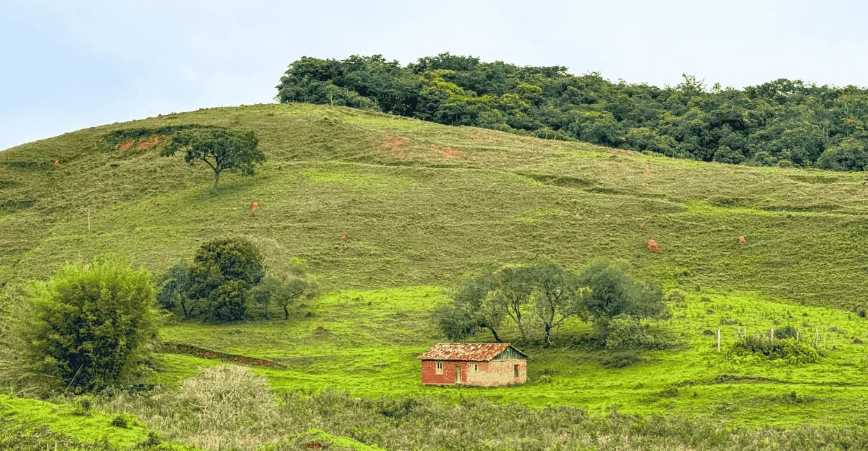 Paisagem rural em Bichinho MG com pequena casa, morros verdes e vegetação típica do interior
