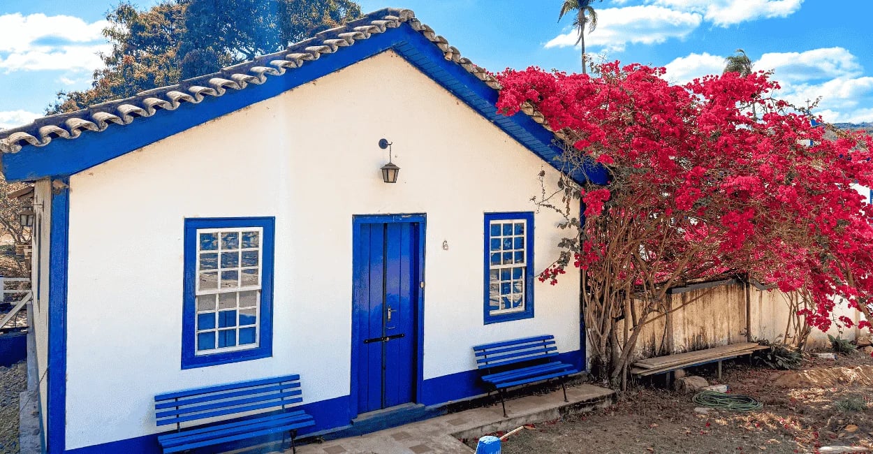 Casa de cor branca e azul, com árvore florida ao lado, na Vila do Biribiri em Diamantina MG
