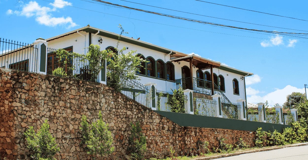 Casarão histórico branco, janelas e portas verdes, acima de um muro de pedra, Alfredo Vasconcelos
