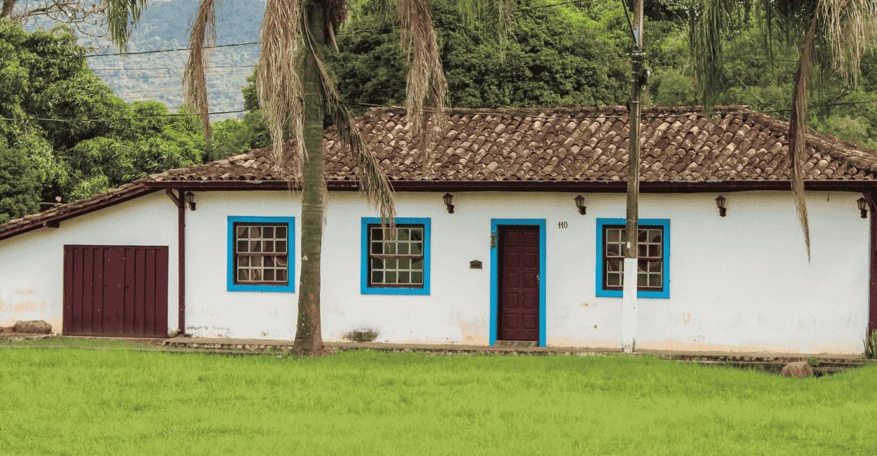 Casa colonial em Brumal MG, com janelas azuis, telhado antigo, palmeiras e gramado verde ao redor