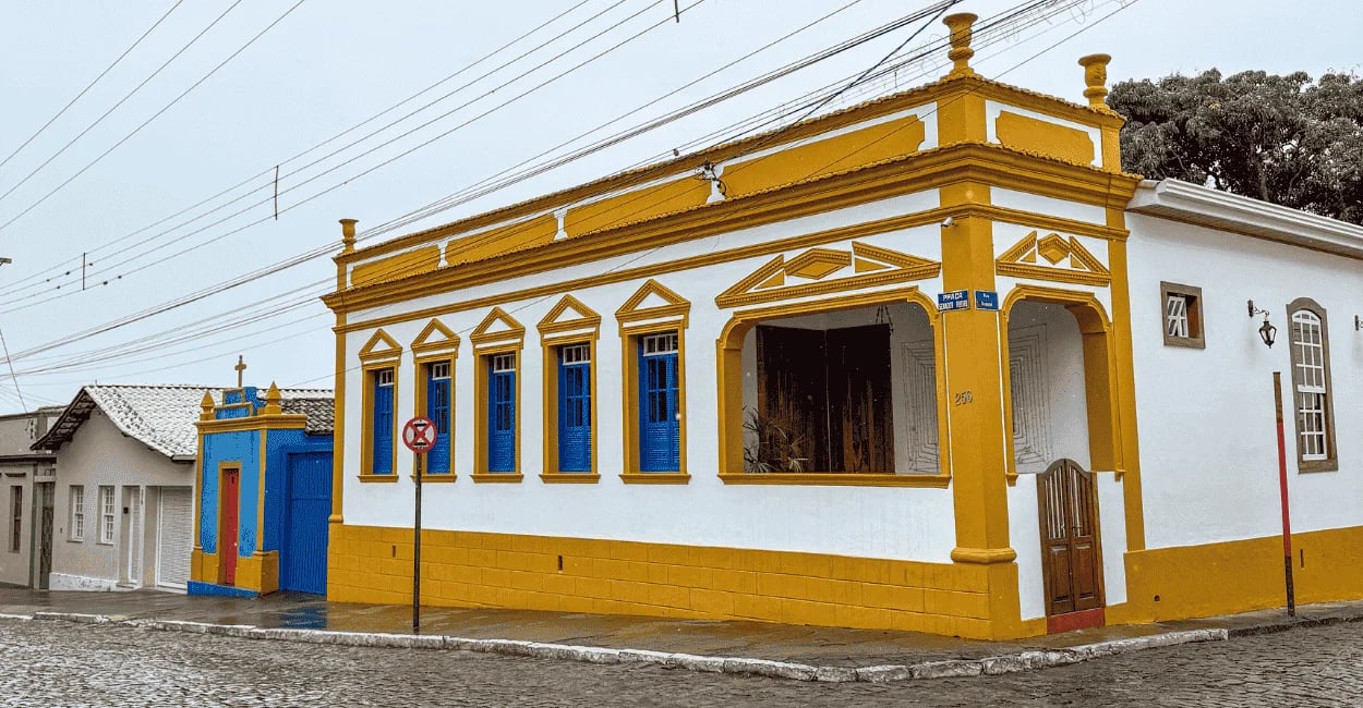 Casa histórica em Entre Rios de Minas com fachada branca e amarela, janelas azuis e rua de pedras