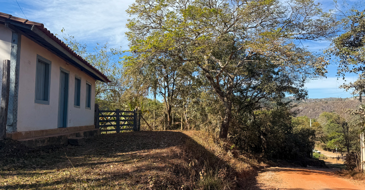 Casa histórica, porteira, árvore e uma estrada de terra em Vau, distrito histórico de Serro MG