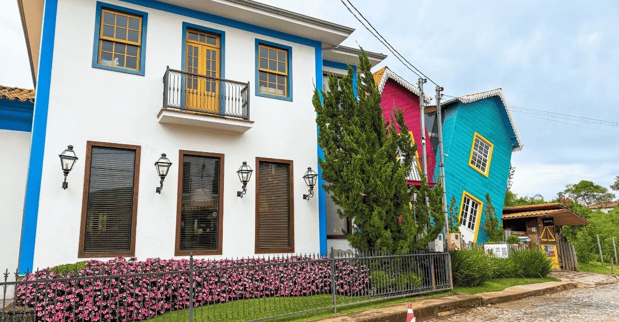Casa Torta em Bichinho, MG, com fachada colorida inclinada ao lado de casarão branco