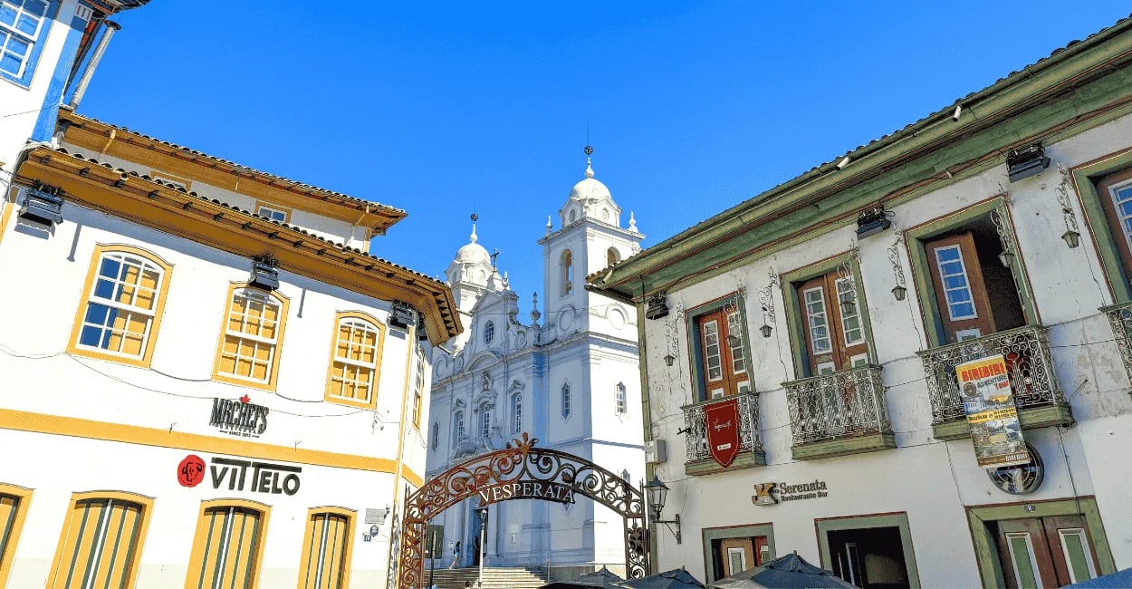 Casarões coloniais em Diamantina emolduram a igreja ao fundo, com o arco da Vesperata sob céu azul