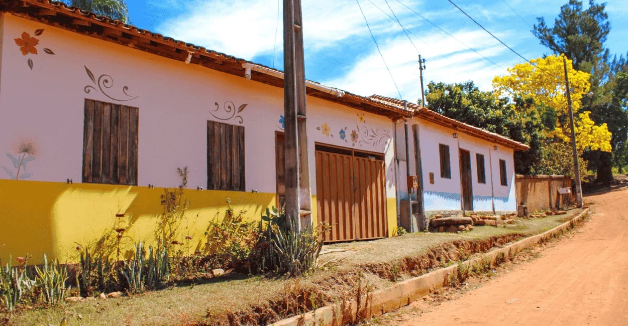 Casas simples, coloridas e decoradas com flores ao longo de uma tranquila rua de terra, Milho Verde