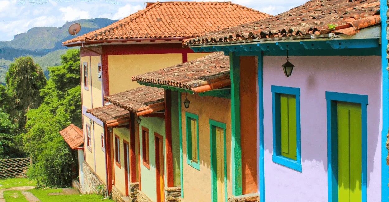 Casas coloniais coloridas em encosta com montanhas ao fundo em Lavras Novas