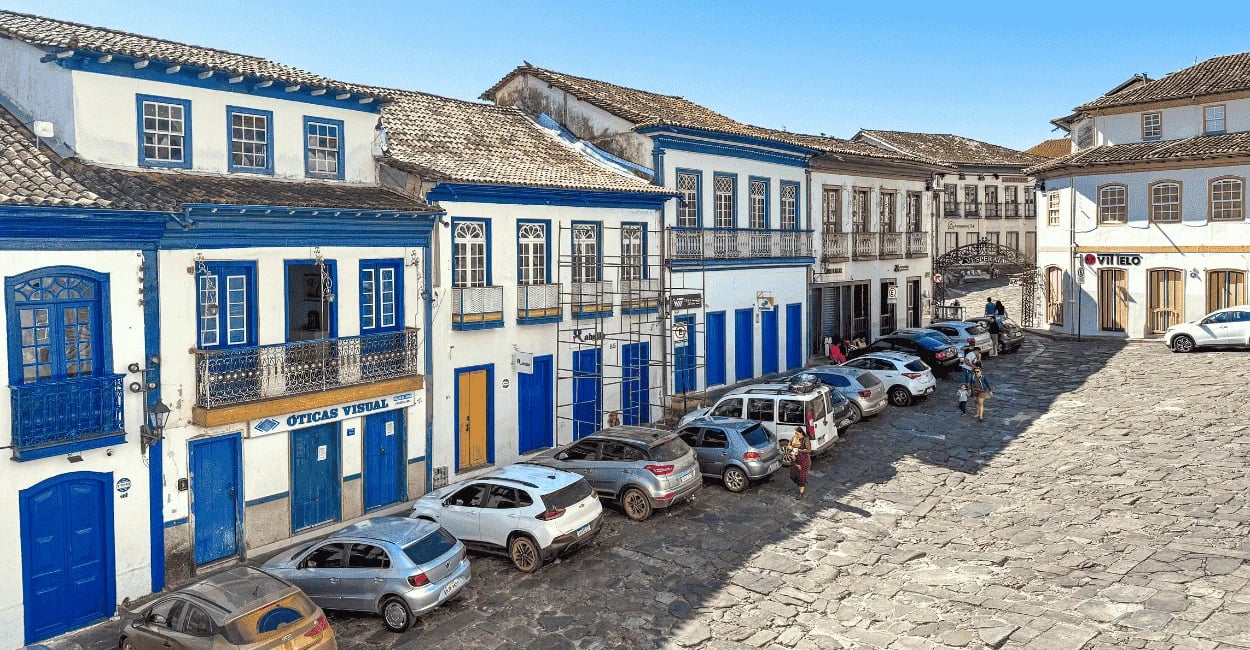 Rua de pedra em Diamantina com casarões coloniais, portas azuis e céu claro ao fundo