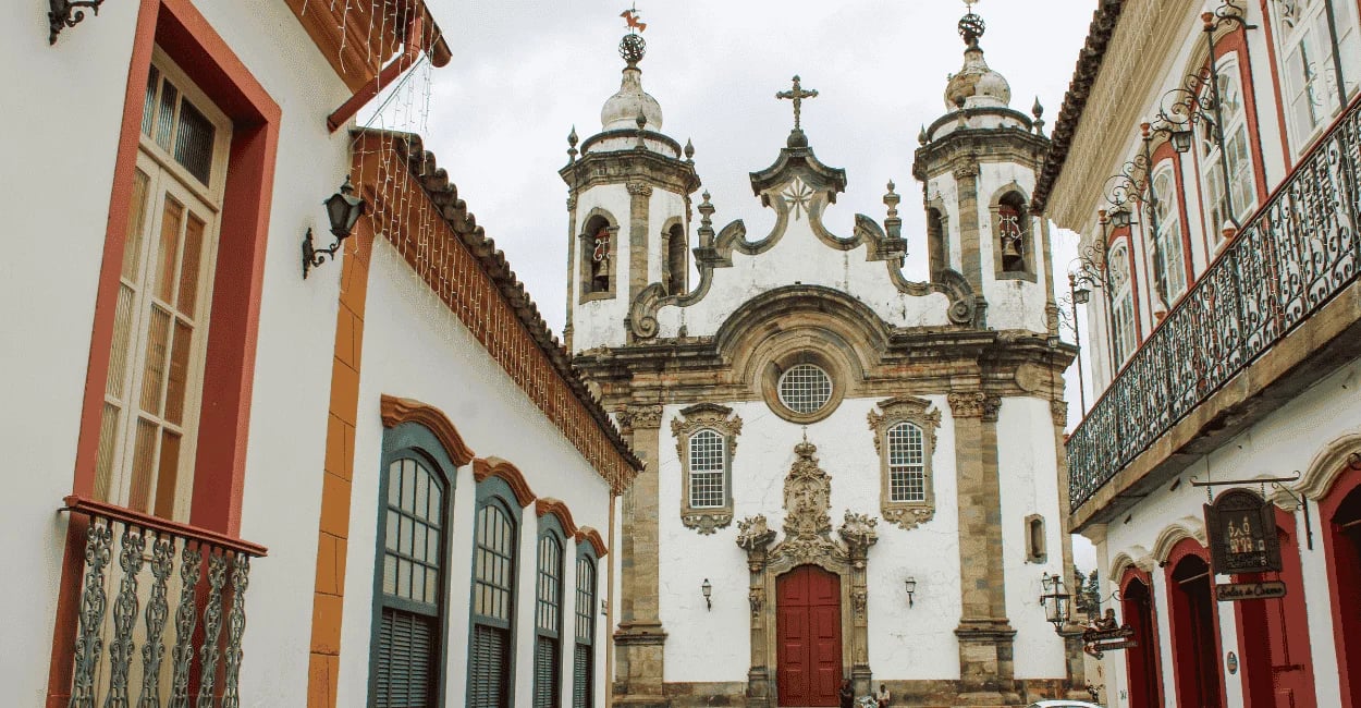 Igreja barroca em São João del-Rei vista entre casarões coloniais, com fachada branca e torres
