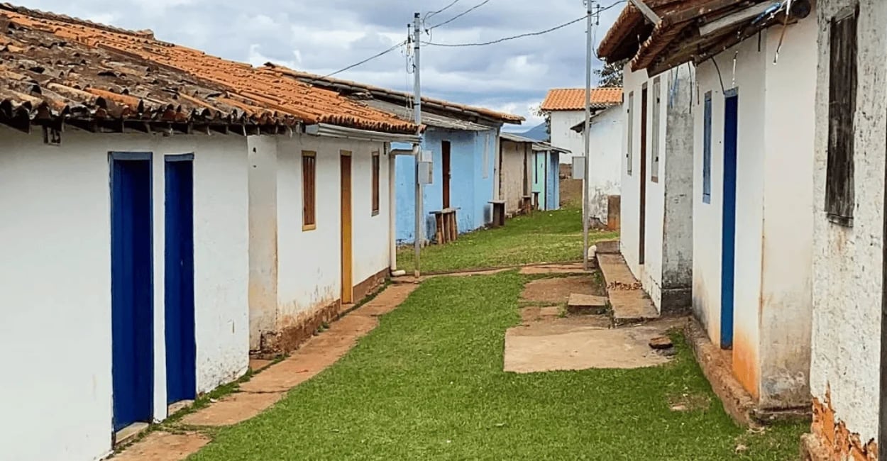 Fileira de casas rústicas com portas azuis em um beco gramado na Serra do Carola, MG