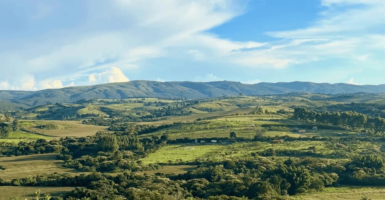 Paisagem rural de Carrancas, MG, com morros ao fundo, campos verdes e vegetação espalhada