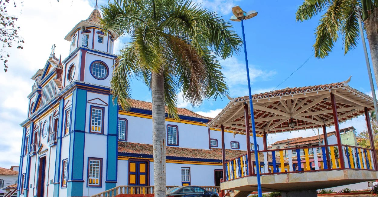 Igreja Matriz e coreto na praça central de Datas, em Minas Gerais, com palmeiras e casario ao redor