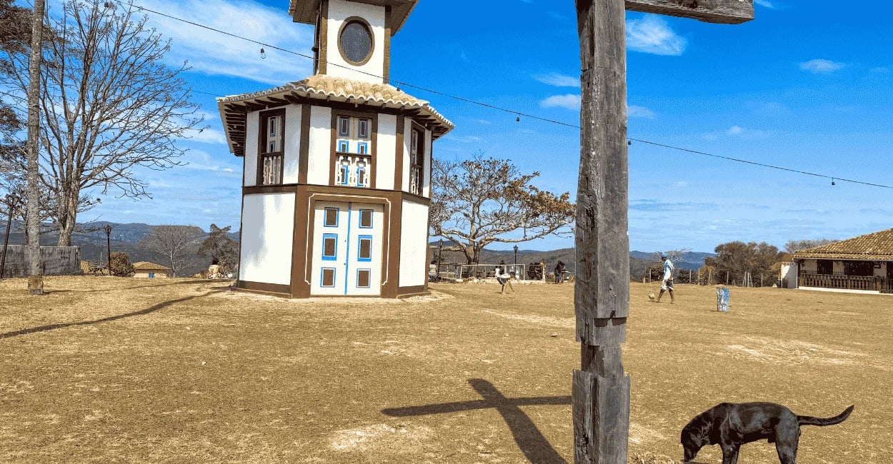 Capela em Milho Verde com cruzeiro de madeira, gramado aberto e céu azul