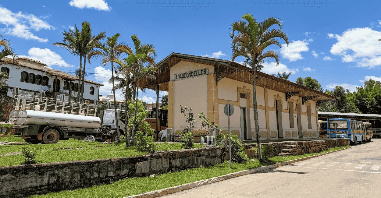 Estação Ferroviaria de Alfredo Vasconcelos, com cores amarelas e céu azul. A frente dela coqueiros