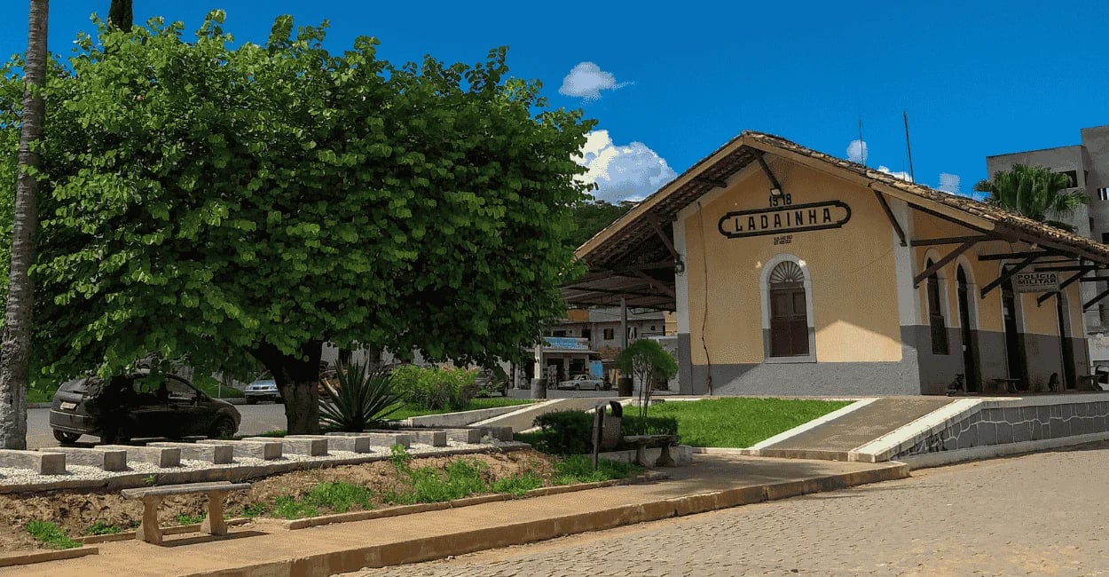 Antiga estação ferroviária de Ladainha, com cor amarela, céu azul e árvore próxima, em Minas Gerais