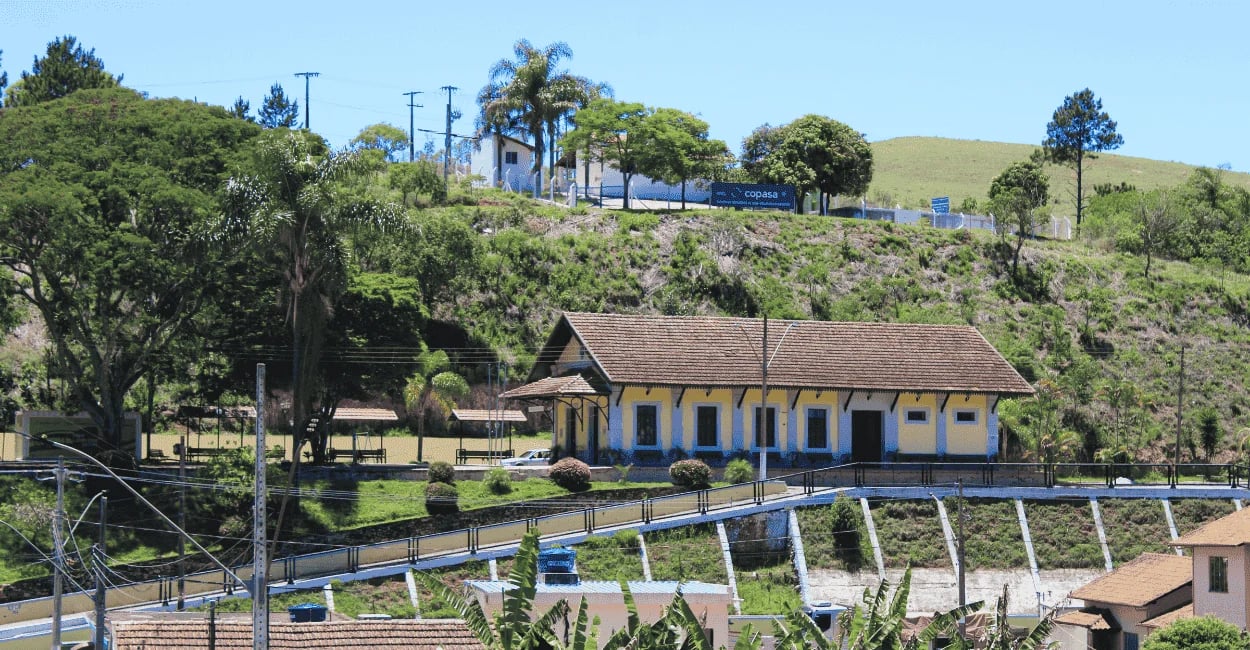 Antiga estação ferroviária amarela e azul cercada por área verde em Ressaquinha, MG