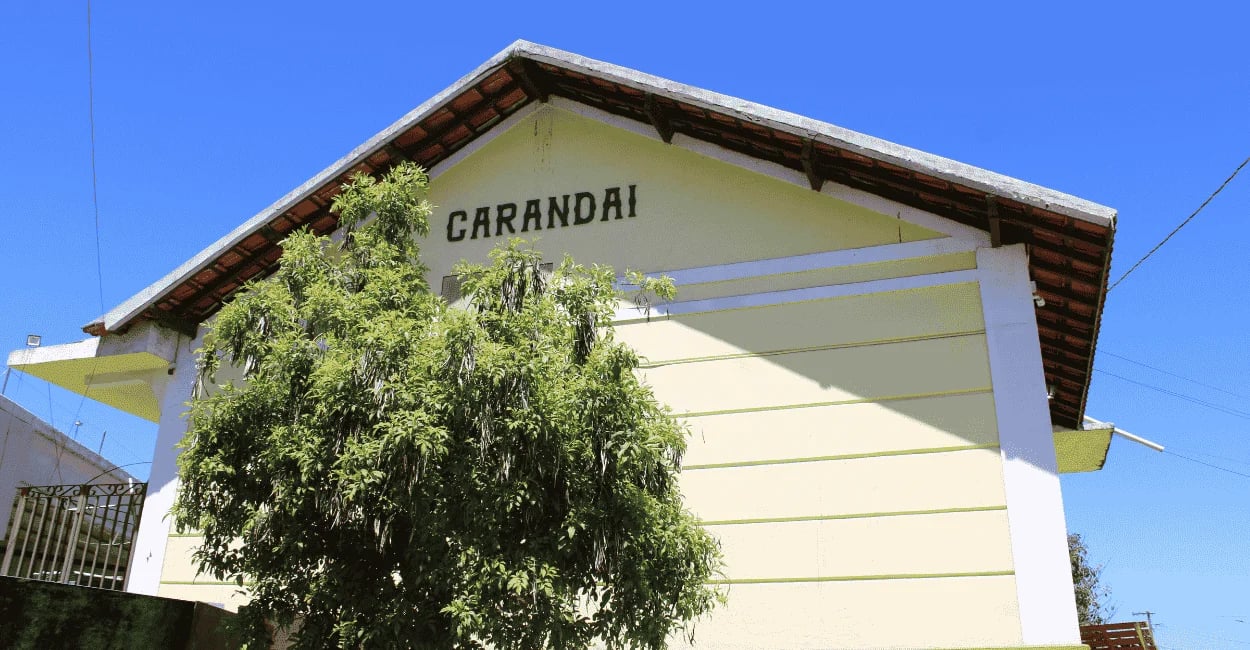 Antiga estação ferroviária de Carandaí com fachada clara, árvore à frente e céu azul
