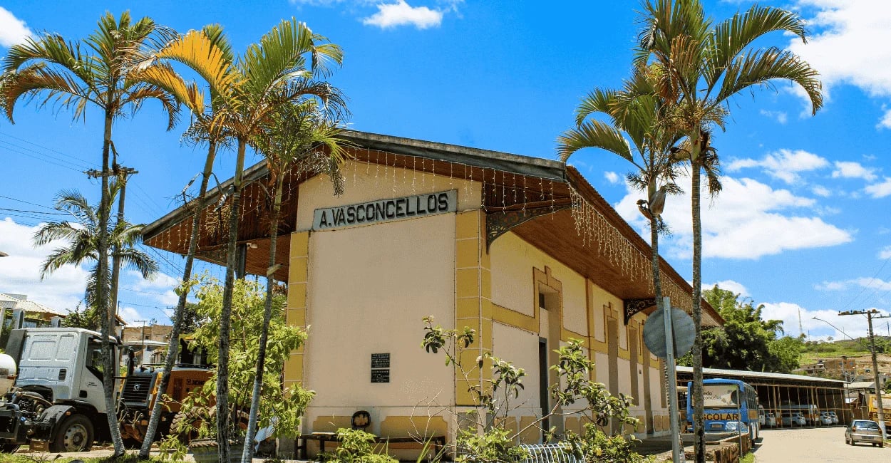 Antiga estação ferroviária de Alfredo Vasconcelos com palmeiras na fachada e céu azul ao fundo
