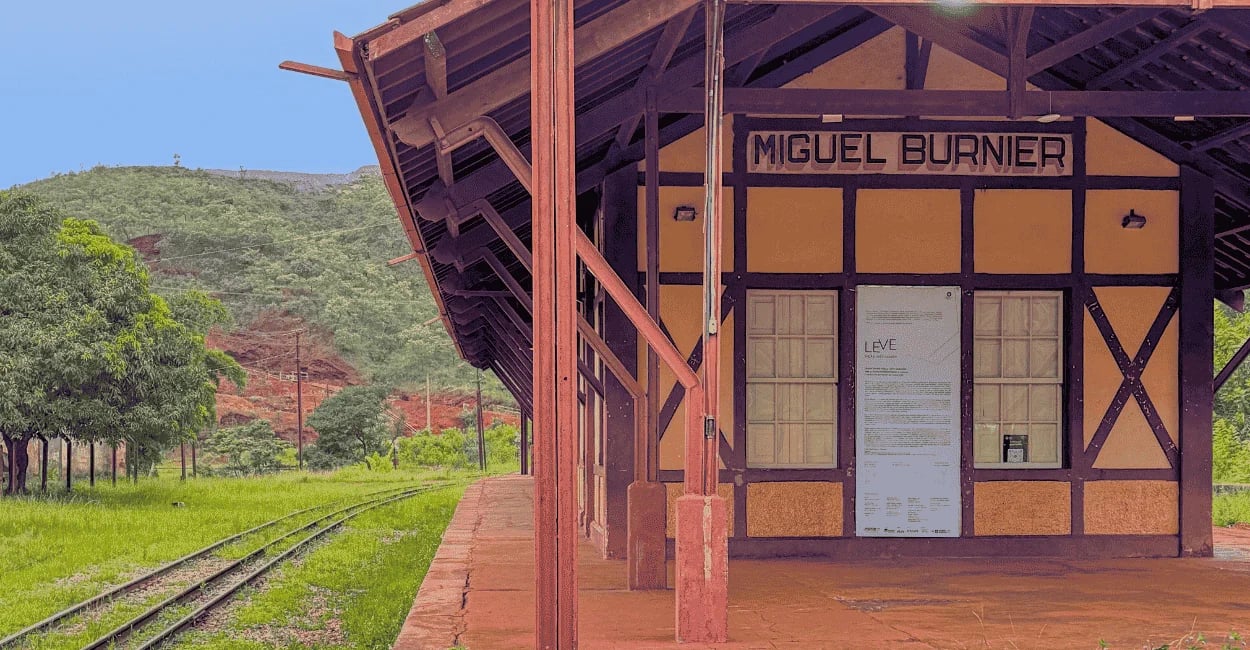 Antiga estação ferroviária amarela e marrom com placa de Miguel Burnier e trilhos cercados por grama