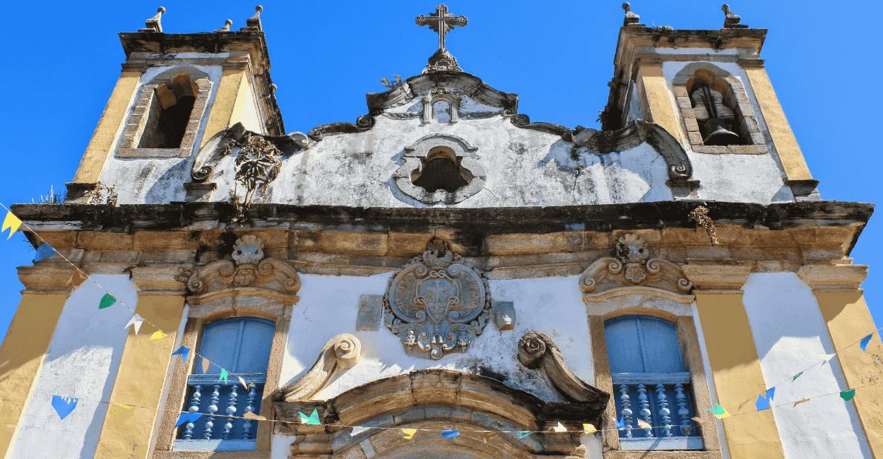 Fachada da Igreja Matriz de Itatiaia MG com torres sineiras, detalhes barrocos e céu azul ao fundo