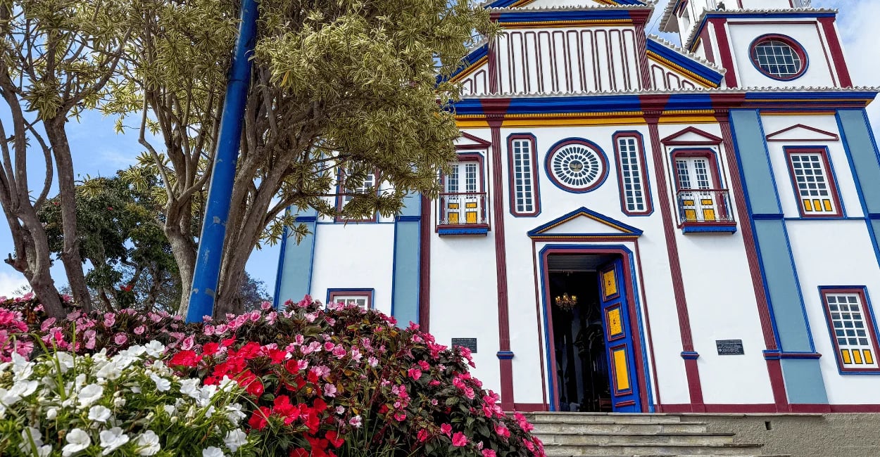 Igreja Matriz de Datas, em Minas Gerais, com fachada colorida, jardim florido e árvores ao redor