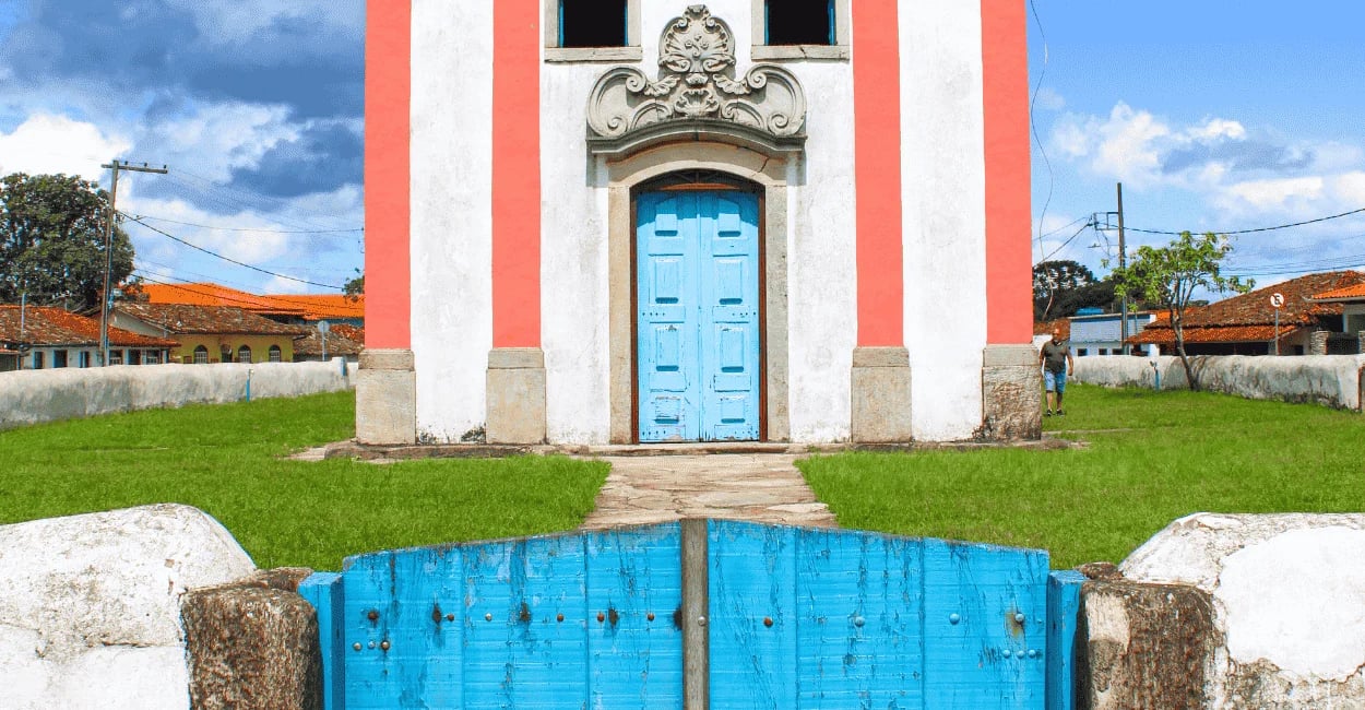 Igreja em Lavras Novas com porta azul, fachada colonial e gramado no entorno